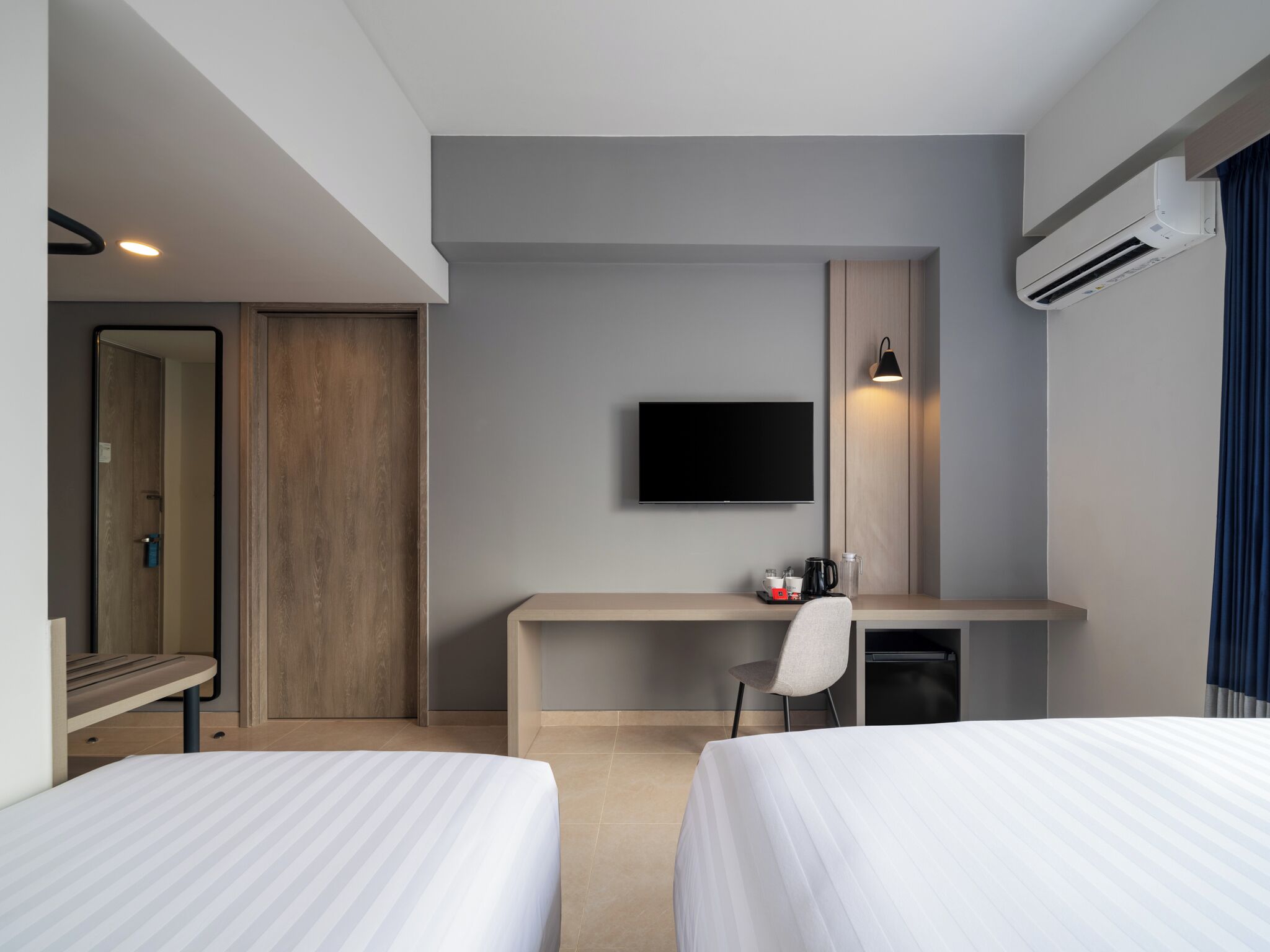 Ett hotellrum med två sängar, ett skrivbord med en stol, en platt-TV, en kaffebryggare och en luftkonditioneringsanläggning.