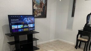 Habitación de hotel con cama, televisor en un mueble, una silla y un cuadro en la pared.