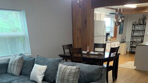 Una sala de estar con un sofá seccional gris, piso de madera y un comedor con mesa y sillas.
