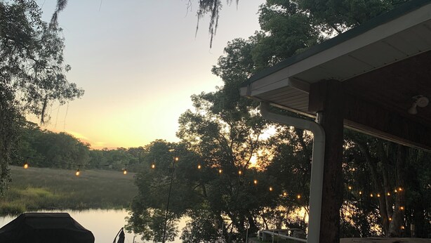Un espacio al aire libre techado con luces colgantes, una parrilla y vista al lago al atardecer.