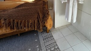 Makuuhuoneessa on puinen sänky, suuri punottu pääty, seinälle ripustettu kylpytakki ja lattiavalaisin.