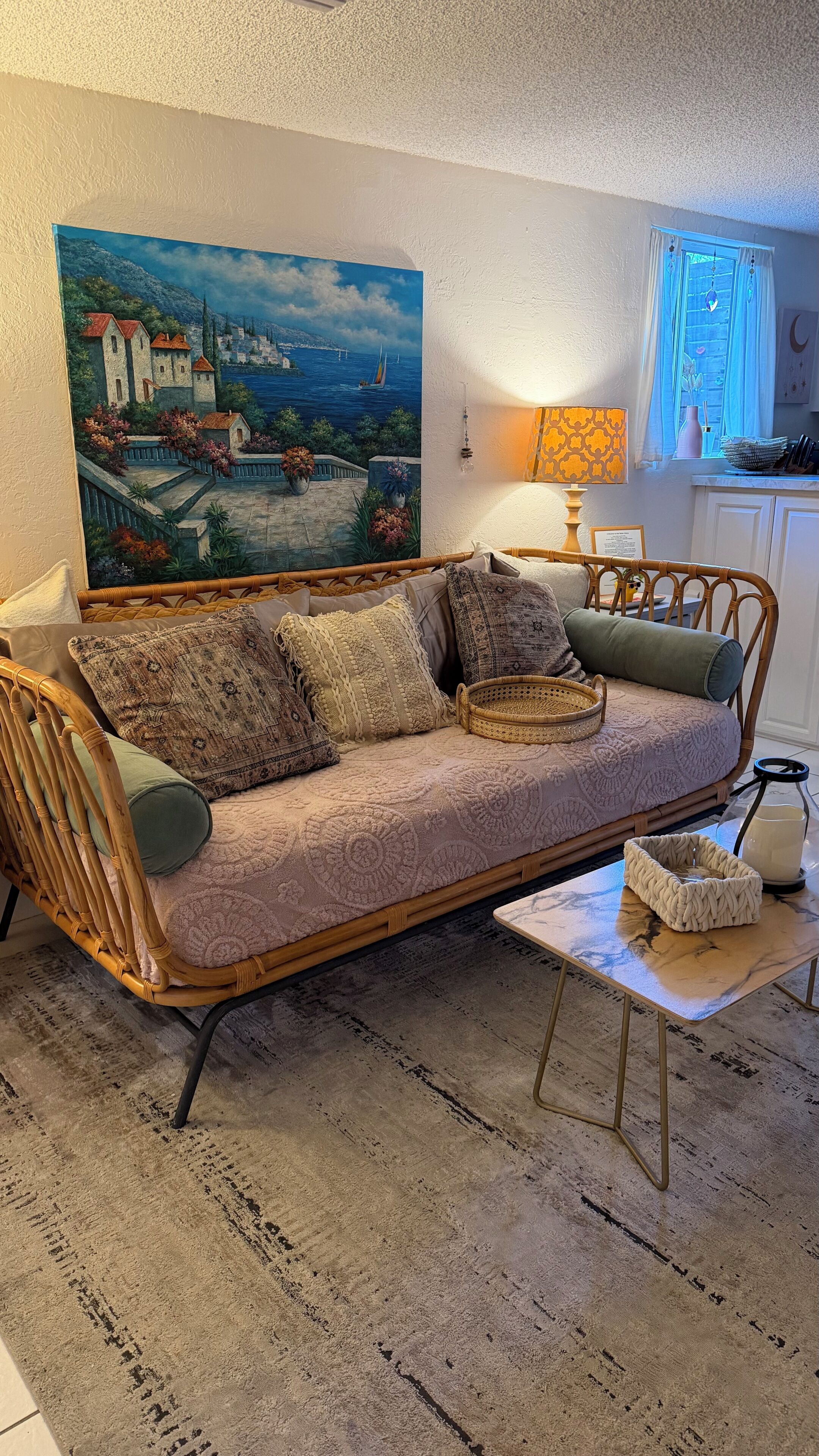 A cozy living room with a sofa, cushions, a coffee table, and a painting of a coastal scene.
