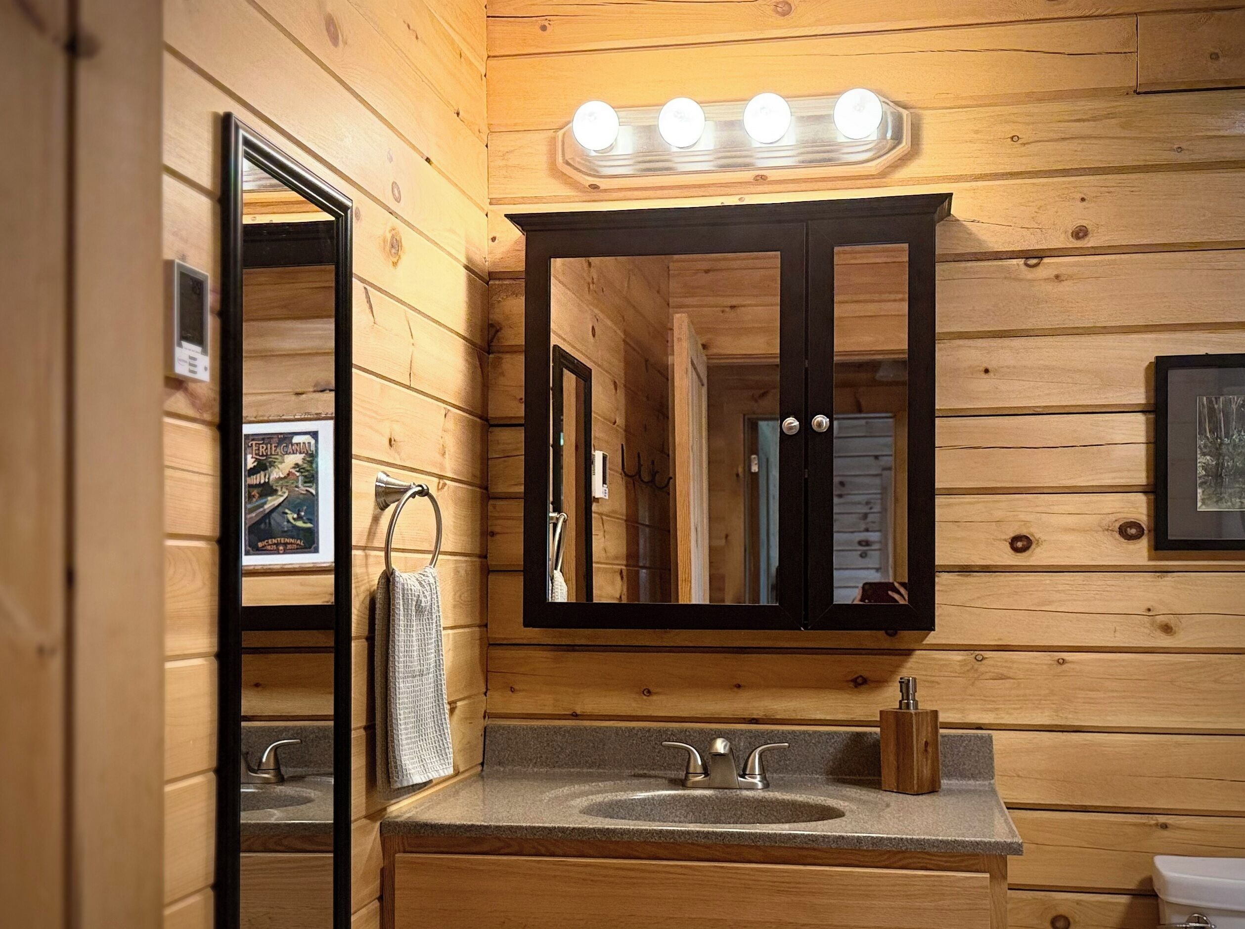 A wooden cabin-style bathroom with a sink, mirror, and overhead lights.