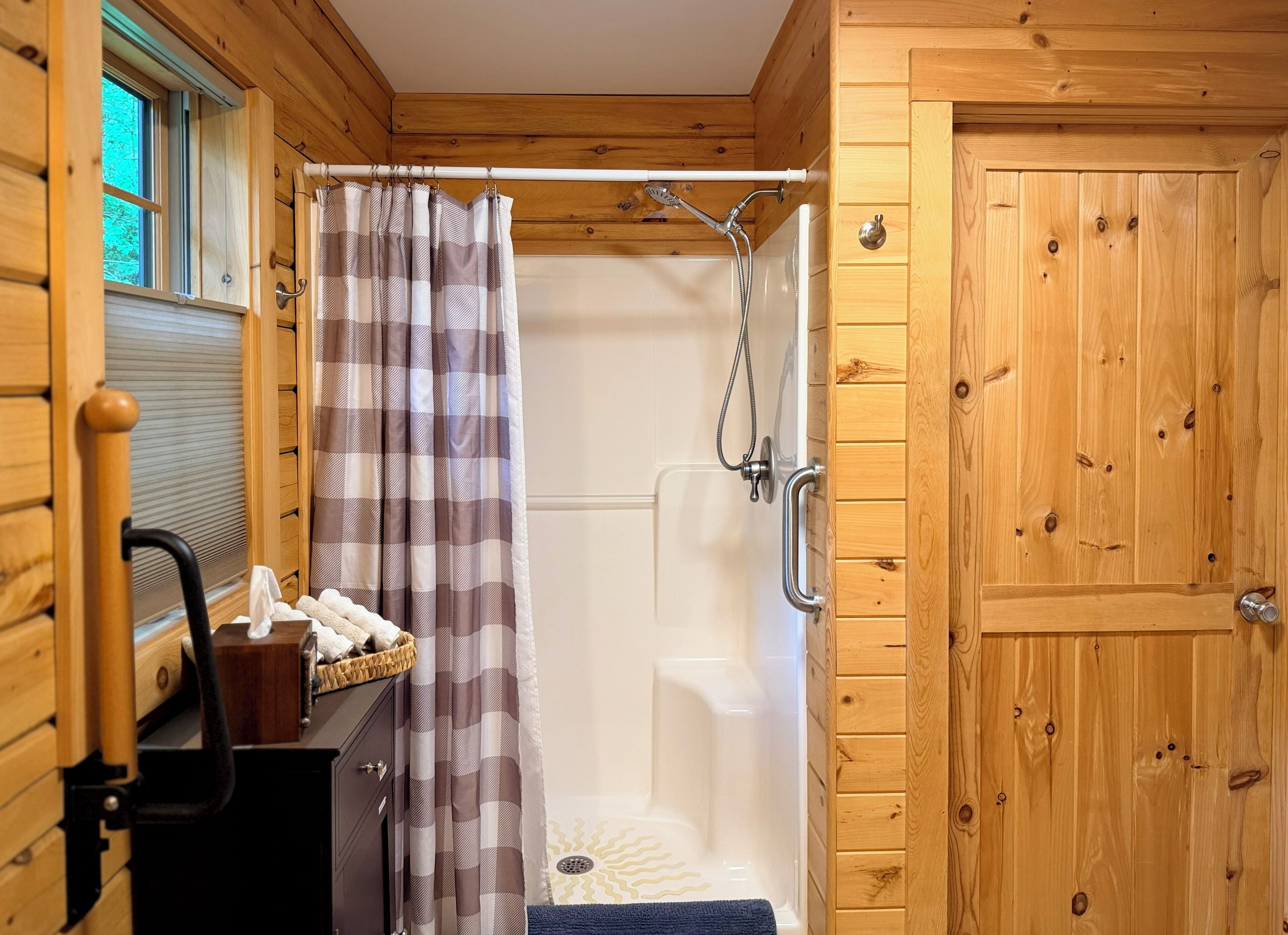Baño de cabaña de madera con ducha, un perchero y una ventana.
