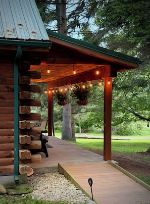 A wooden cabin with a porch, string lights, and a hanging planter.