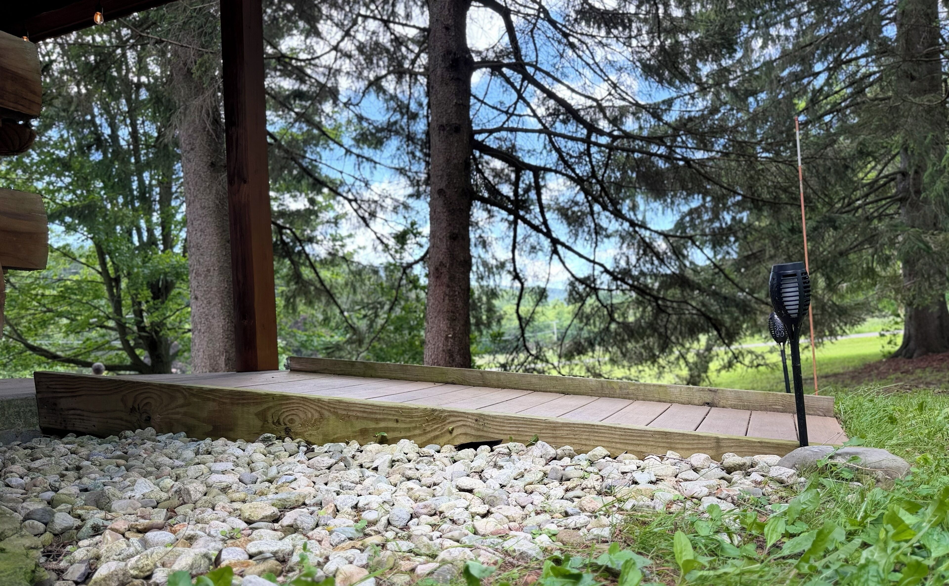 Um deck de madeira com guarda-corpo de metal, rodeado por uma área de cascalho e vegetação.