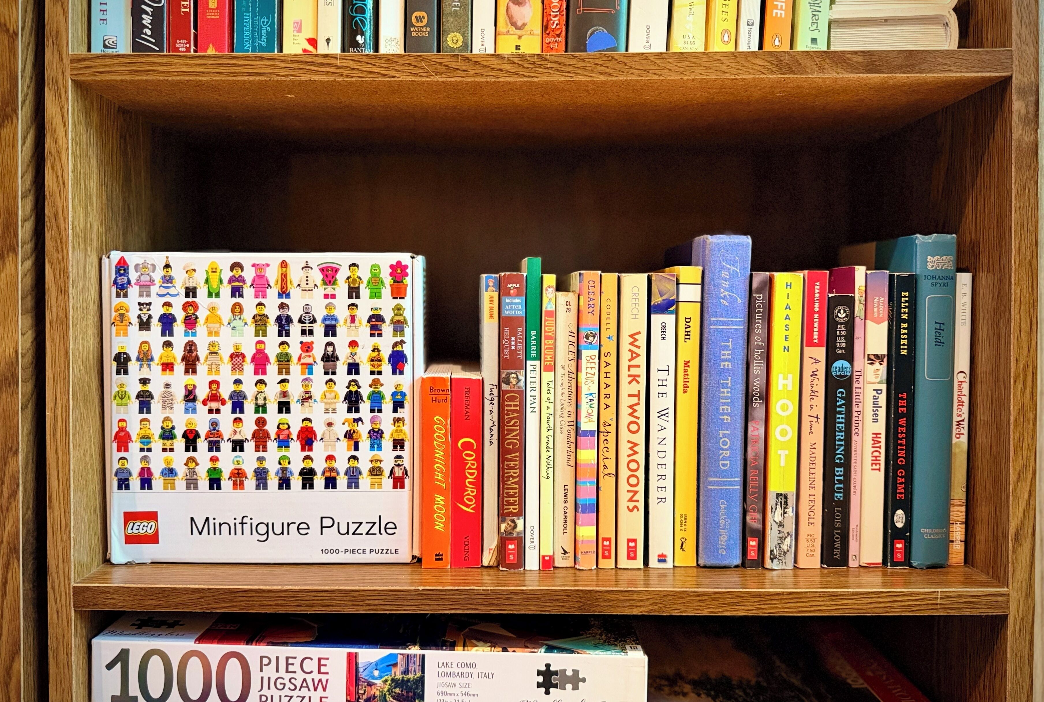 A bookshelf with a variety of books and a LEGO minifigure puzzle box.
