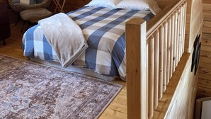A cozy wooden cabin bedroom with a bed, a chair, a small table, and a rug. - Timber Haven - Serene getaway-Fireplace, air conditioning, fire pit, grill, WiFi (Cohocton)