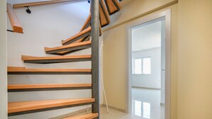 Un escalier moderne avec des marches en bois et des rampes en métal, menant à une pièce lumineuse dotée d’une grande fenêtre et d’une porte.