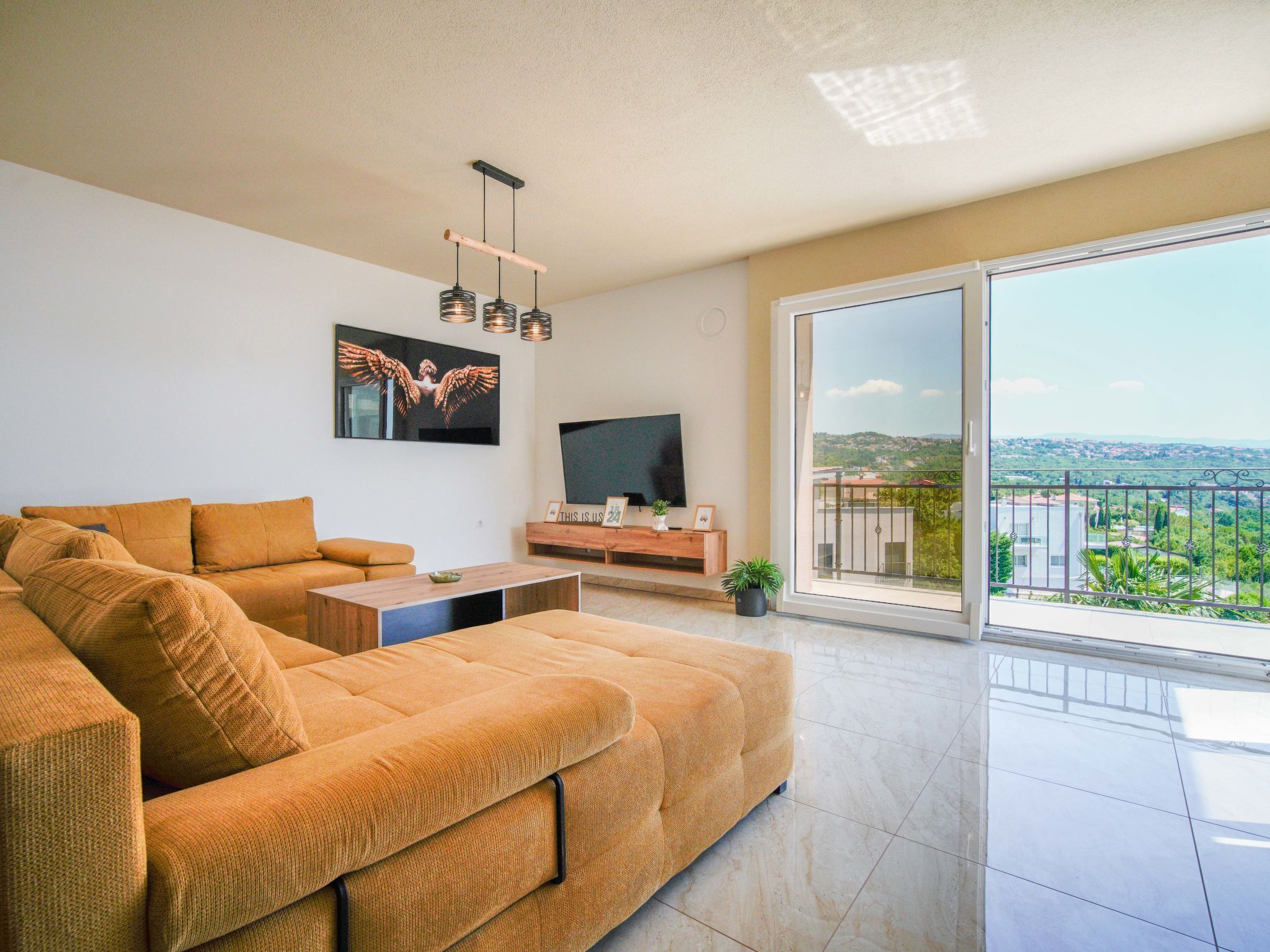Ein modernes Wohnzimmer mit einer großen Couch, einem Couchtisch, einem Flachbildfernseher und einem Balkon mit Blick auf die Stadt.
