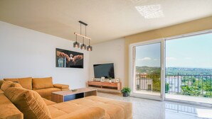 Un salon moderne doté d’un grand canapé, d’une table basse, d’un téléviseur à écran plat et d’un balcon offrant une vue sur la ville.