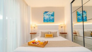 Une chambre d’hôtel avec un grand lit, des tables de chevet, un plateau avec le petit-déjeuner et des œuvres d’art accrochées aux murs.