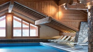 Une piscine intérieure avec des poutres en bois et un mur en pierre.