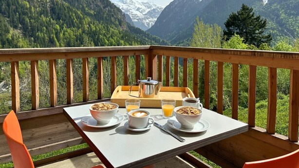 Une terrasse en bois avec une table dressée pour le petit-déjeuner, offrant une vue sur un paysage montagneux.
