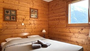 Une chambre dans un chalet en bois, avec deux lits, une fenêtre donnant sur la montagne et des œuvres d’art décoratives sur les murs.