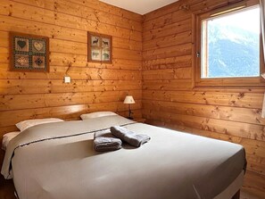 Een houten kamer met twee bedden, een raam met uitzicht op de bergen en decoratieve wanddecoratie.