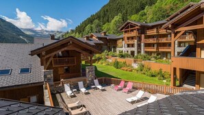 Un complexe hôtelier comprenant plusieurs bâtiments en bois, une terrasse en bois avec des chaises longues et une vue sur les montagnes.
