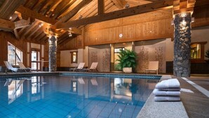 Une piscine intérieure aux carreaux bleu clair, dotée de chaises longues et de piliers en pierre.