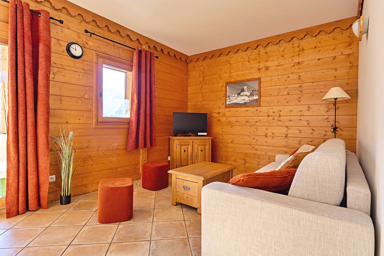 Une pièce chaleureuse avec des murs en bois, un canapé, une télévision, un meuble et une fenêtre avec des rideaux.