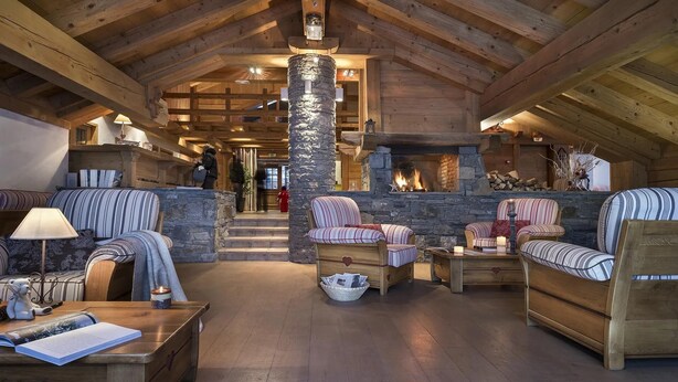 L’intérieur chaleureux d’un chalet avec une cheminée en pierre, des meubles en bois et un plafond haut.