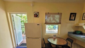 Uma cozinha compacta com geladeira, uma mesa de jantar com cadeiras, uma janela com persianas e uma porta que dá para o exterior.