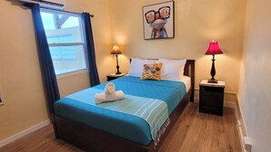 Quarto de hotel com cama, duas luminárias de cabeceira, janela com cortinas, ar condicionado fixado na parede e um quadro.