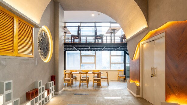Ein modernes Interieur mit gewölbter Decke, Wänden aus Holzlamellen, einer zentralen Sitzecke mit Tischen und Stühlen sowie einem großen Fenster mit Blick auf die Stadt.