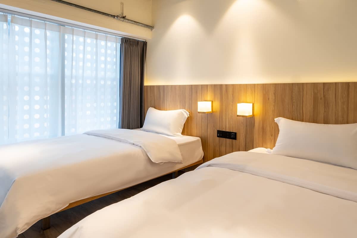 A hotel room with two beds, a wooden headboard, and two wall-mounted lights.
