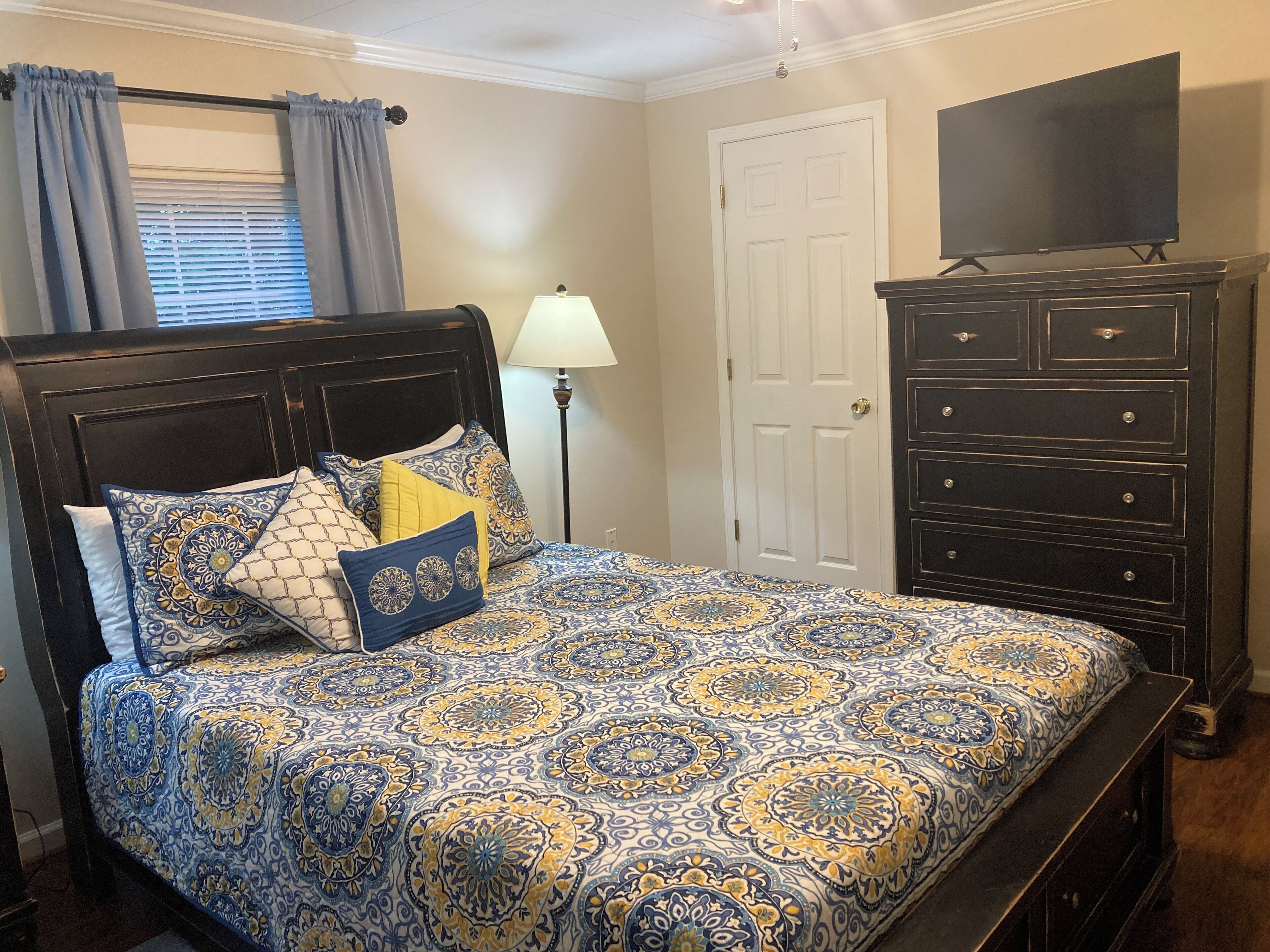 A bedroom with a bed, a dresser, a television, and a lamp.