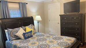 Une chambre à coucher avec un lit, une commode, un téléviseur et une lampe.
