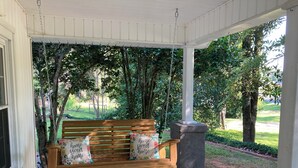 Un banc en bois agrémenté de coussins à motifs floraux et un pilier en pierre, installés sur un porche avec un tapis bleu.
