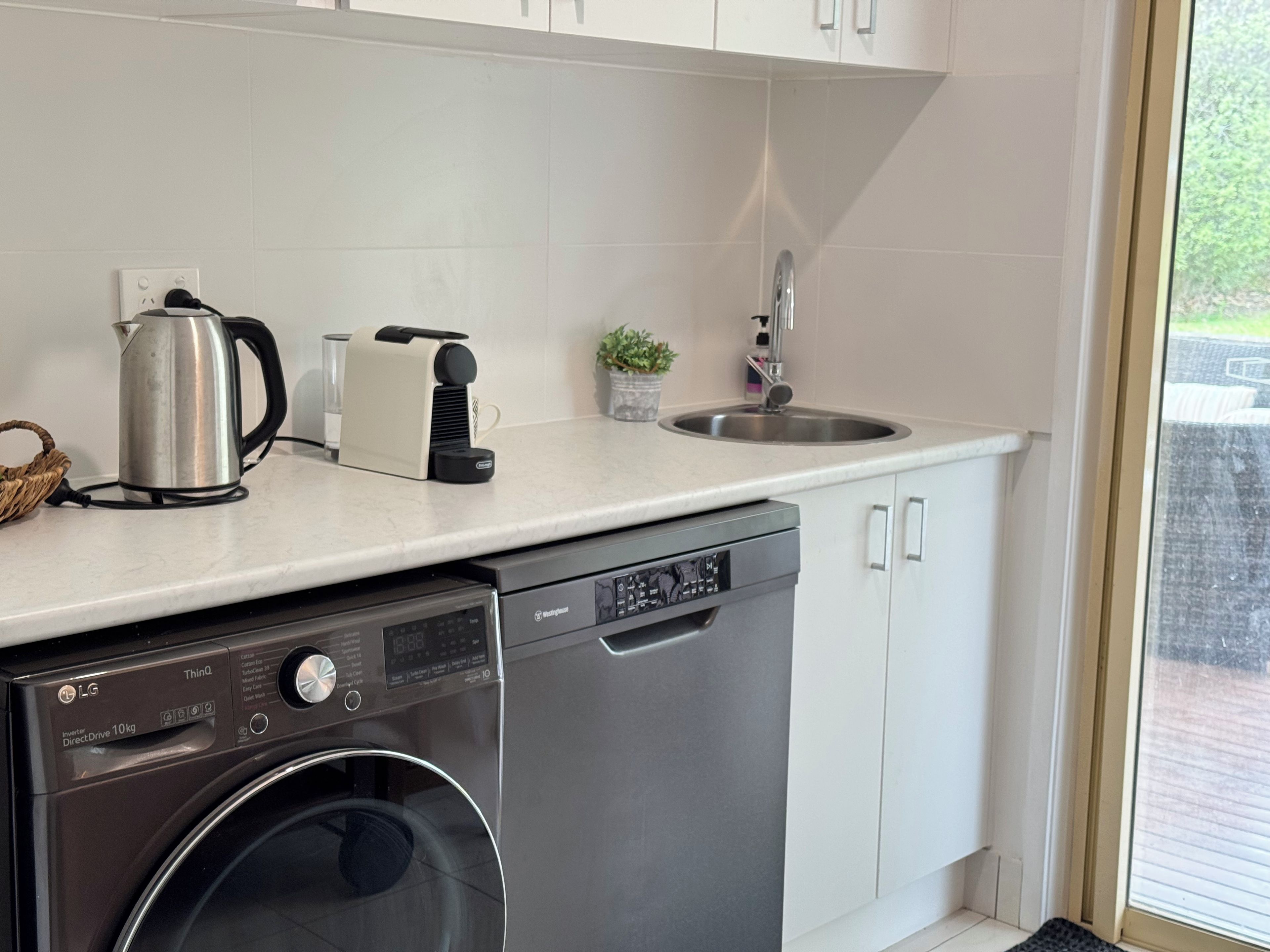 Une cuisine compacte équipée d’un lave-vaisselle, d’une machine à café et d’une bouilloire posés sur le plan de travail.