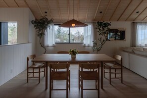 A dining area with a wooden table and chairs, a hanging light fixture, and large windows with views of trees. - Boots Off Collection (Hakuba)
