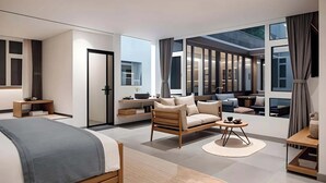 A modern bedroom with a large bed, a sofa, and a dining table. There are large windows and a view of the outside.