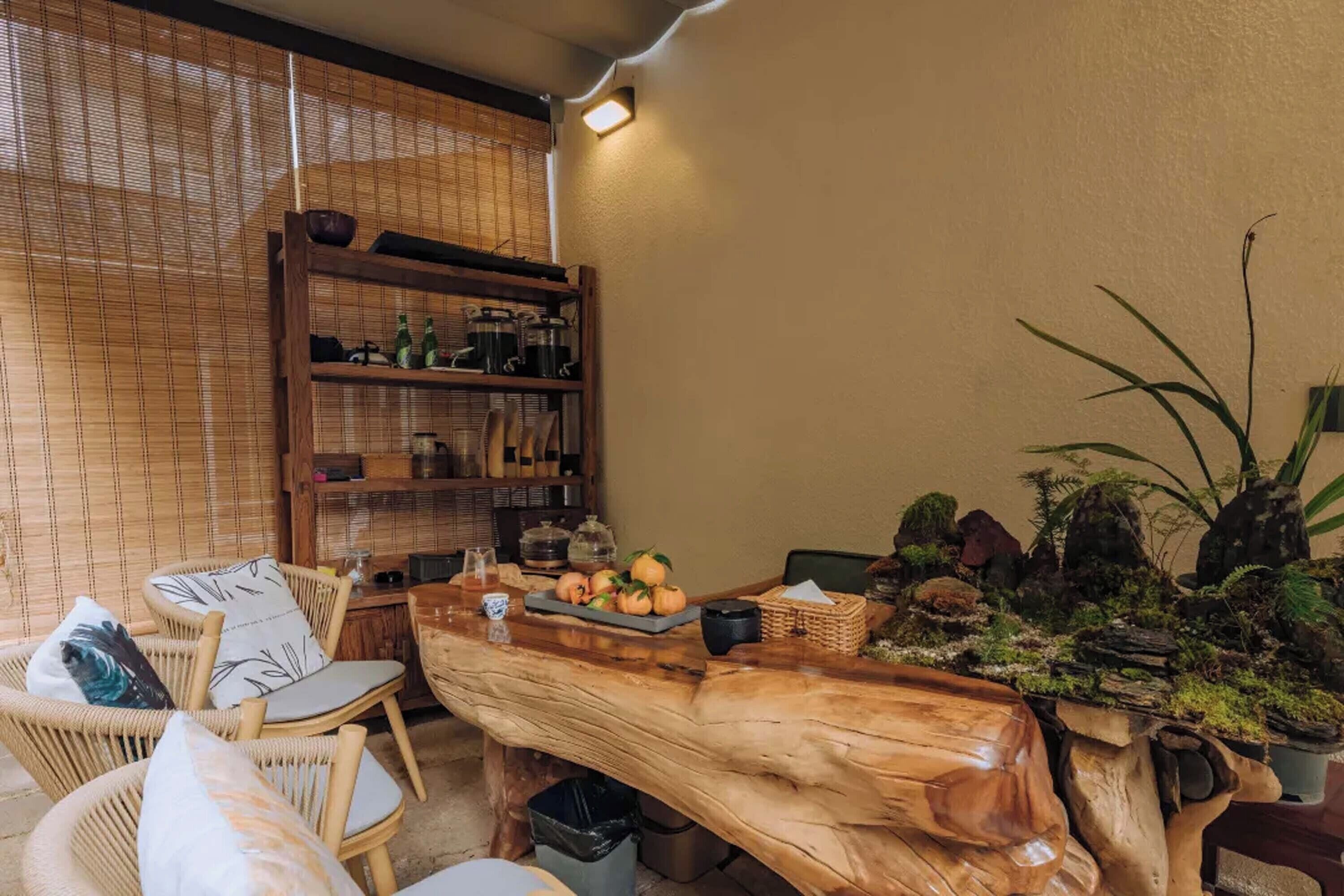 A cozy dining area with wicker chairs, a wooden table, and a shelf with kitchen items.