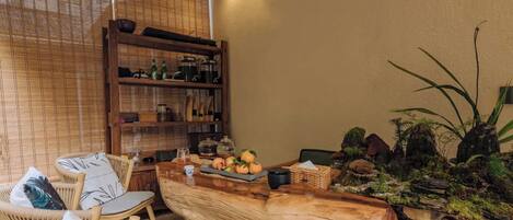 A cozy dining area with wicker chairs, a wooden table, and a shelf with kitchen items.