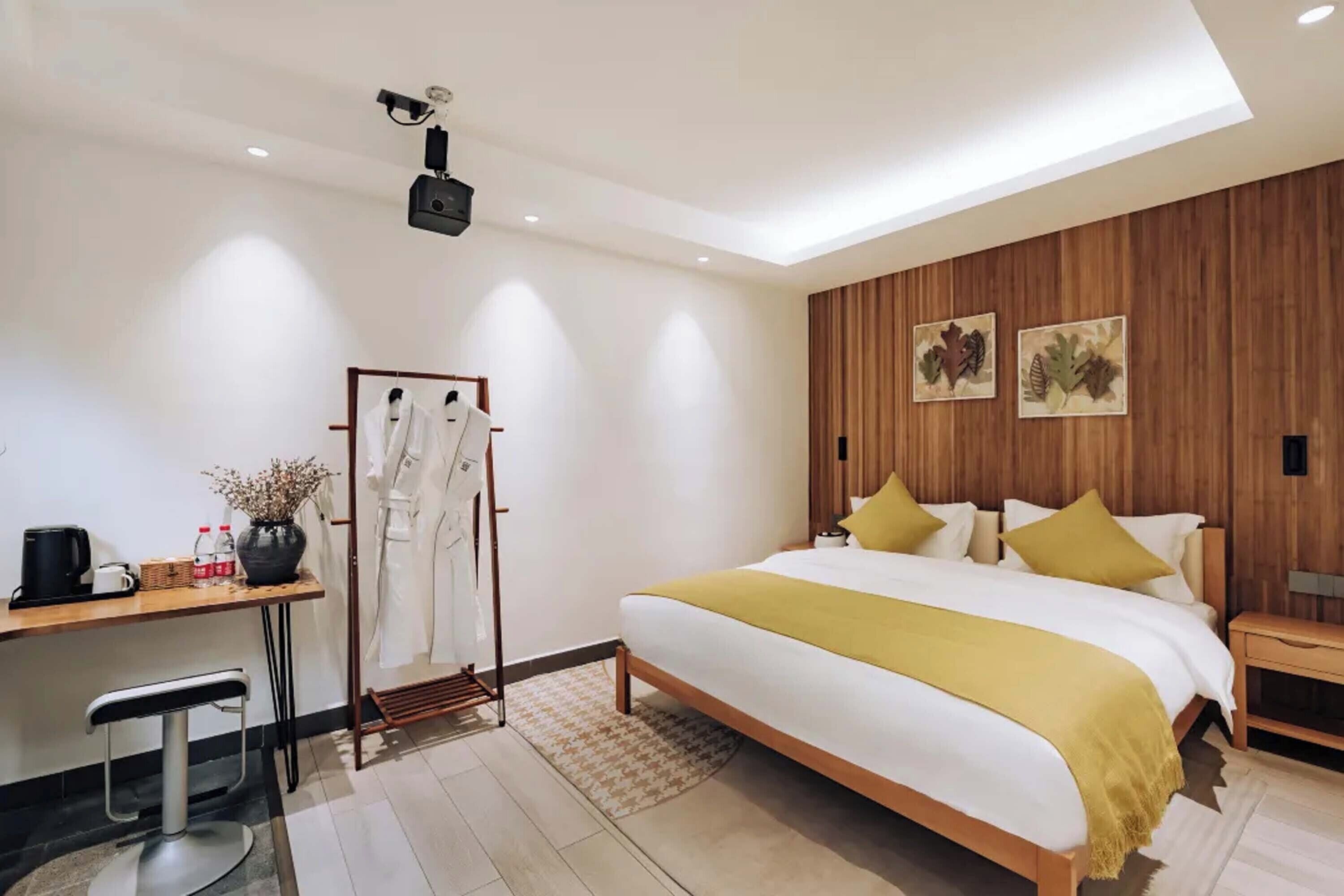 A modern hotel room with a large bed, a desk with a chair, a vanity, and a shower area.