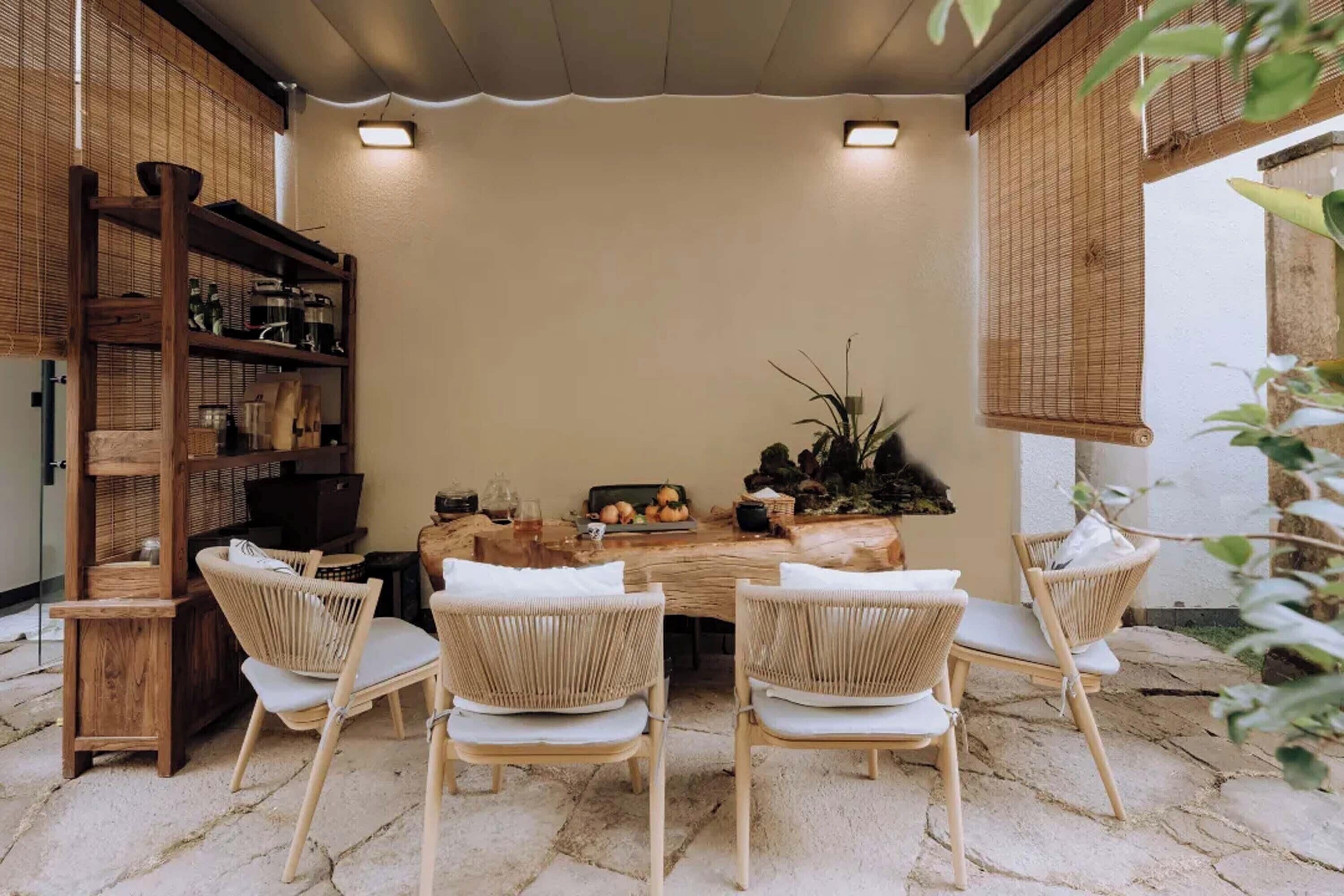Uma área de refeições com uma mesa de madeira rústica, cadeiras de vime e diversos objetos sobre a mesa.