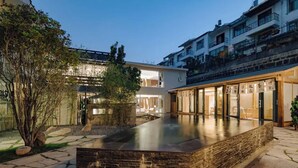 A modern building with a flat roof, large windows, and a stone pathway leading to a rectangular pool area.