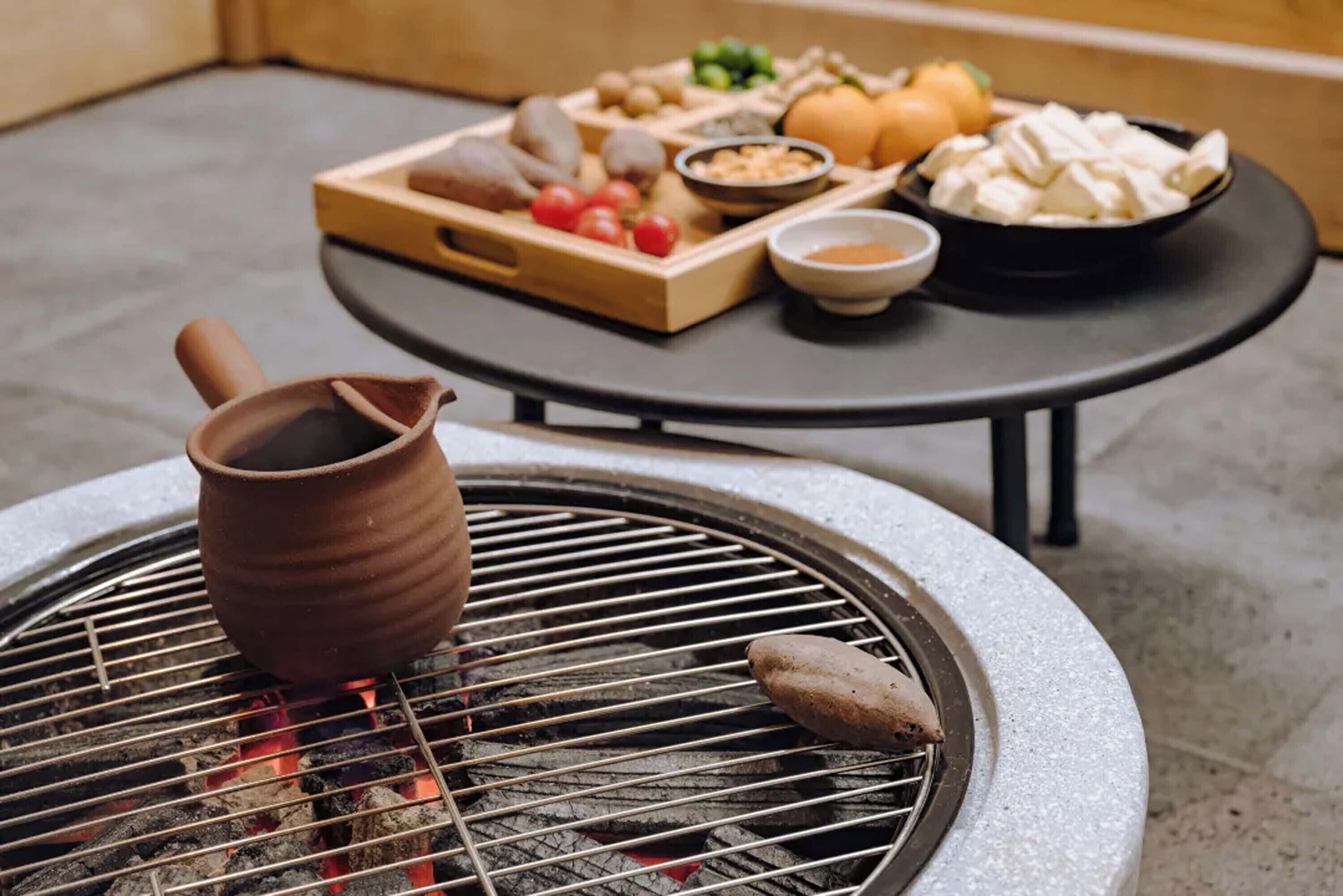 Una parrilla redonda de carbón con una jarra de cerámica y un pincho de madera.