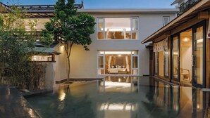A modern building with a reflective pool in the center, surrounded by trees and a wooden structure.