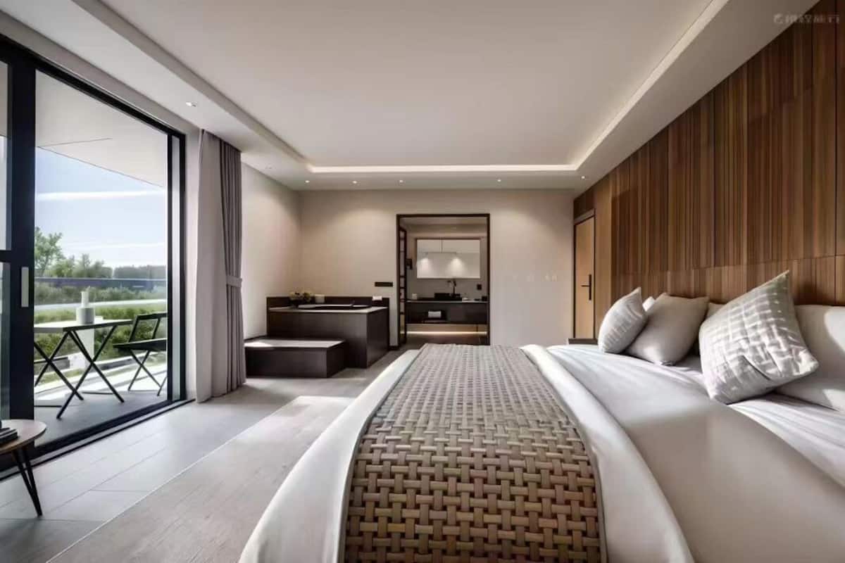 A modern bedroom with a large bed, a small desk, and a view of the outdoors.