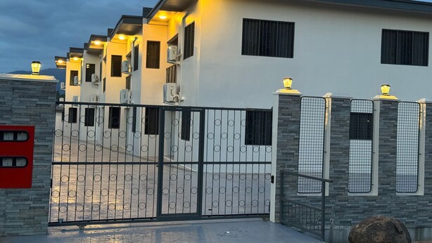 Una casa moderna de dos pisos con entrada protegida por un portón, unidades de aire acondicionado y fachada de piedra.