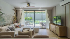 Un soggiorno moderno con divano, poggiapiedi e televisore su un mobile in legno.