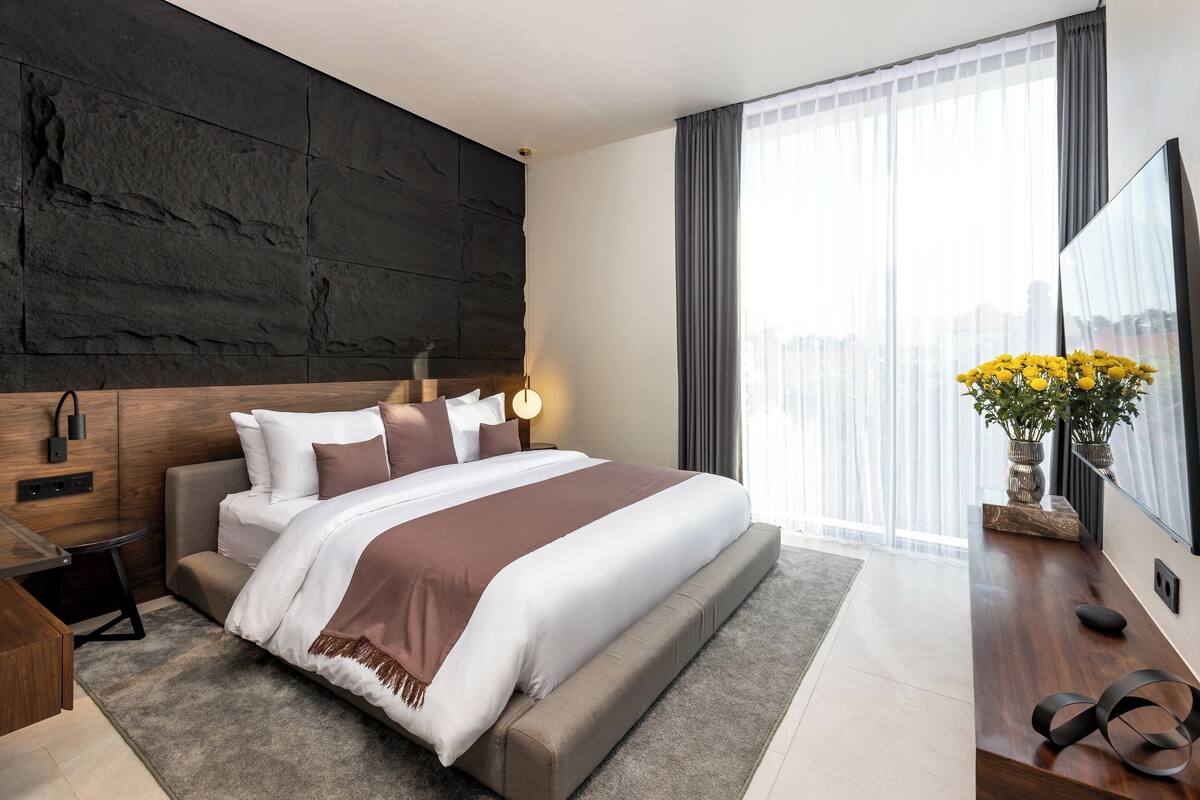 Una habitación de hotel moderna con una cama grande, un escritorio y un ventanal con cortinas.