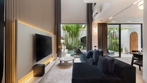 Een moderne woonkamer met een flatscreen televisie, een zwarte bank en een salontafel. Er is een groot raam met uitzicht op een tuin.
