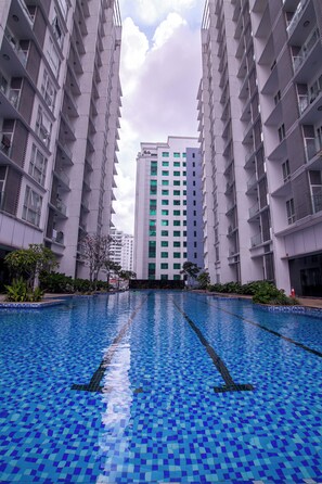 A swimming pool with blue mosaic tiles, surrounded by high-rise residential buildings.