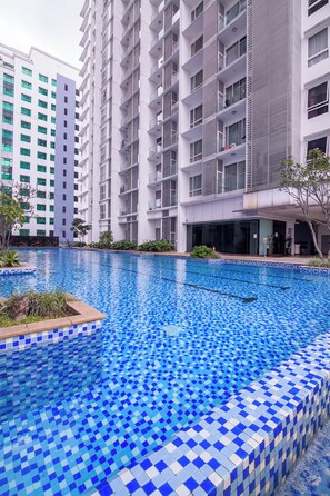 A swimming pool with blue mosaic tiles, surrounded by a modern building with balconies and a glass facade.