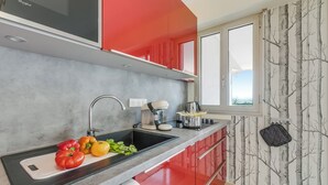 A modern kitchen with a black countertop, red cabinets, and a window with a tree wallpaper. - Studio Near Beach, Sea View & Garage, Antibes, France (Antibes)