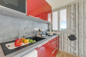 Une cuisine moderne avec un plan de travail noir, des placards rouges et une fenêtre ornée d’un papier peint représentant des arbres.